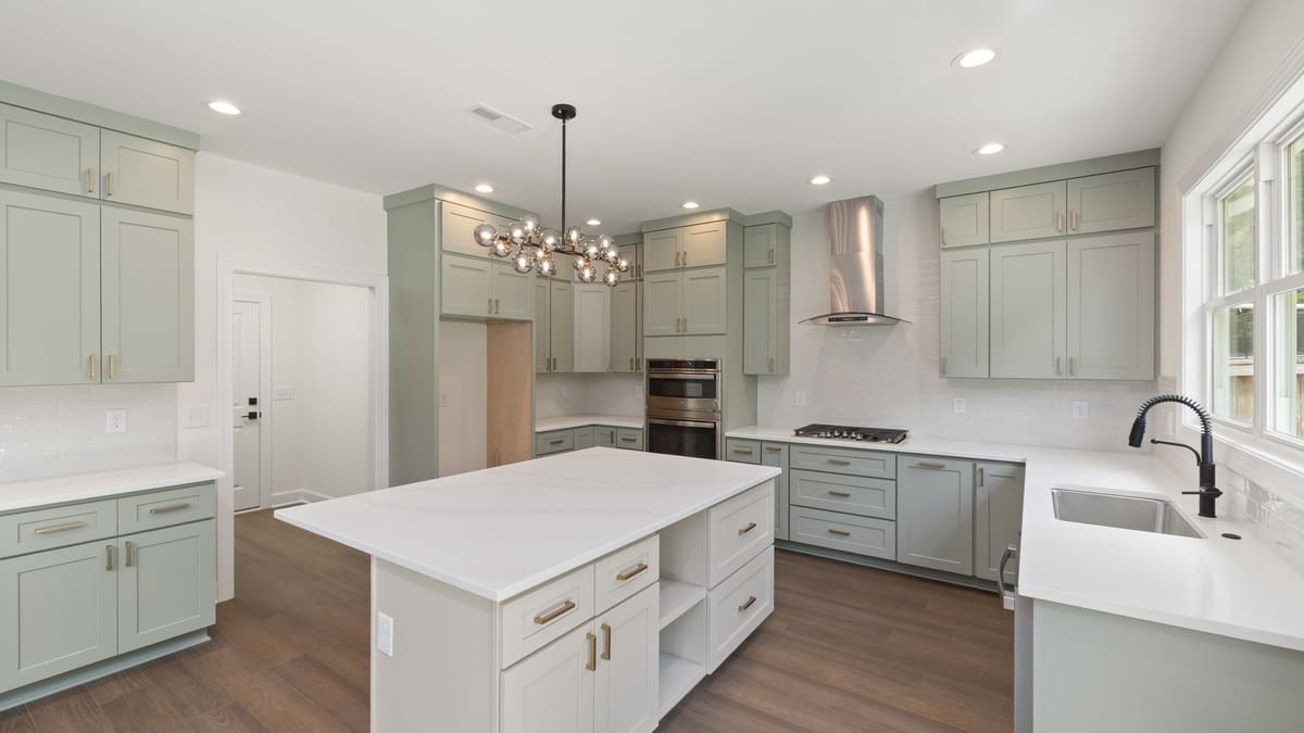 Kitchen with sage-green Shaker cabinets, a white island, and a stainless range hood