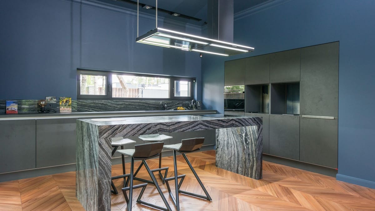 Custom kitchen with a marble waterfall island, dark full-height cabinetry, and a herringbone wood floor