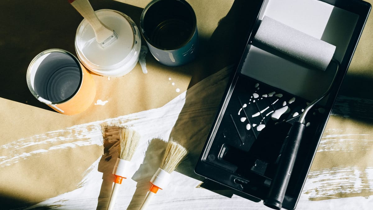 Paint roller in a tray beside brushes and open paint cans on a paper drop cloth
