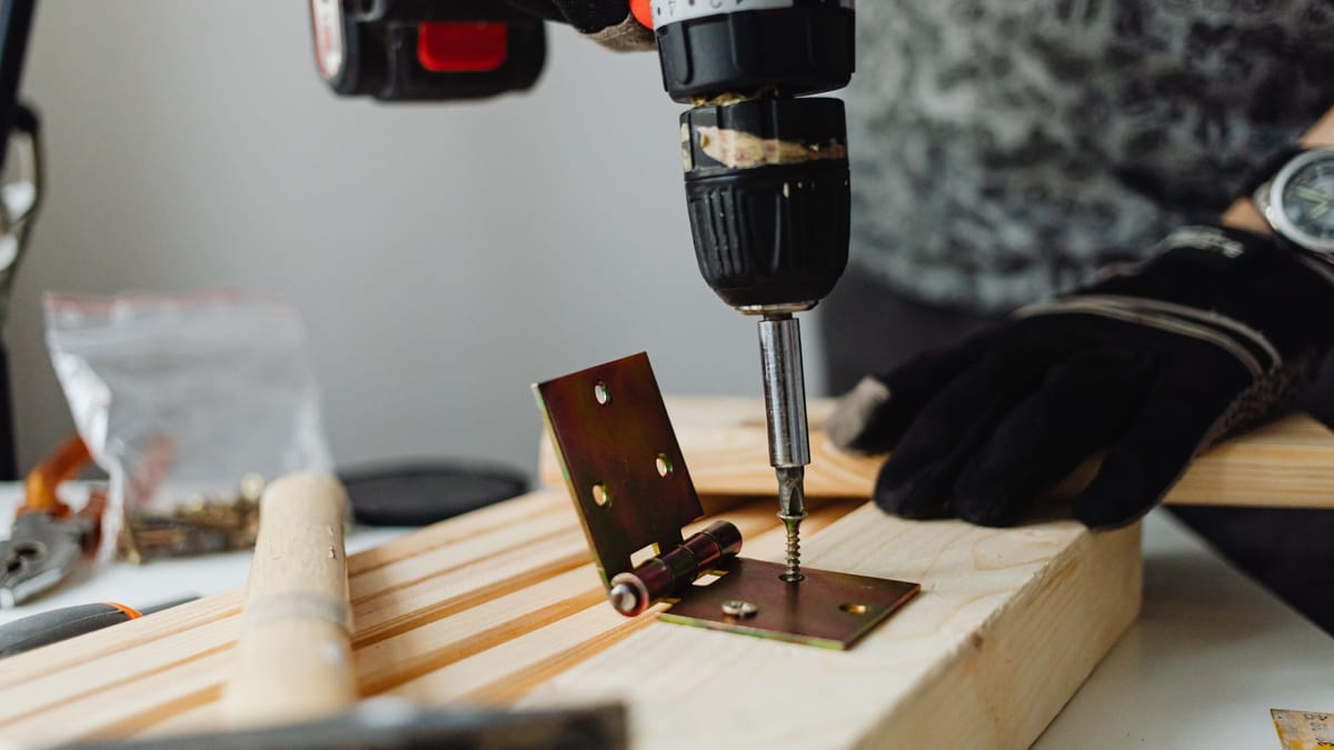 Carpenter fastening a hinge to a wood board with a cordless drill