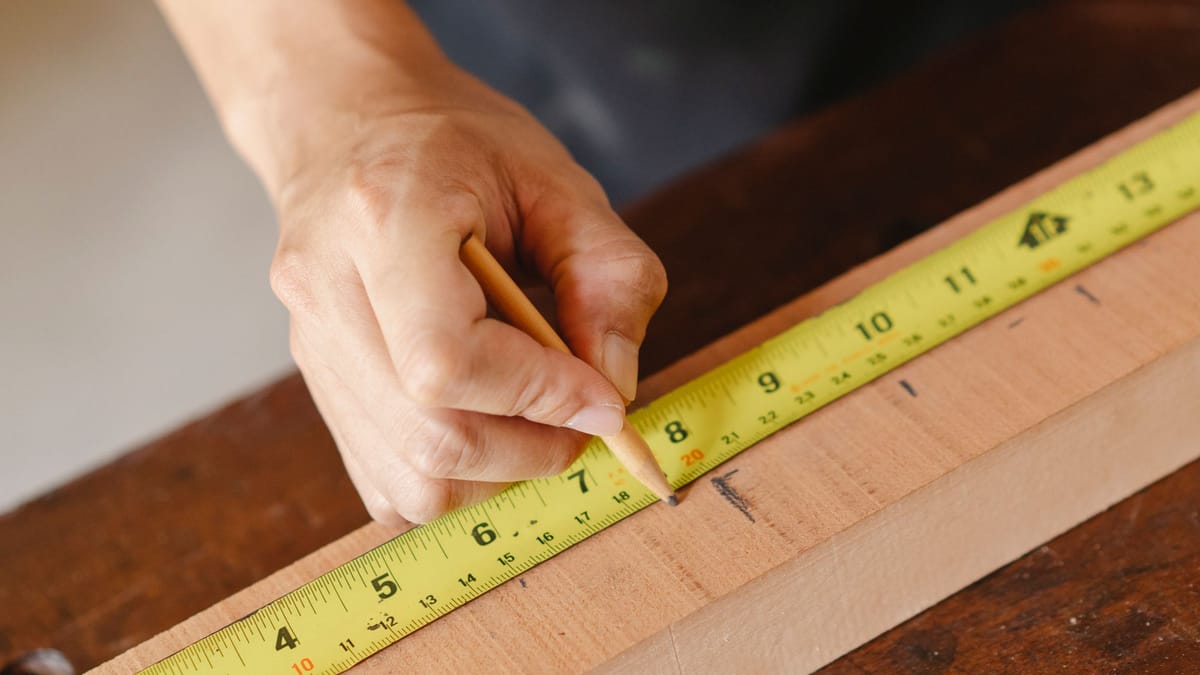 Hand marking a measurement on a wood board with a pencil and tape measure